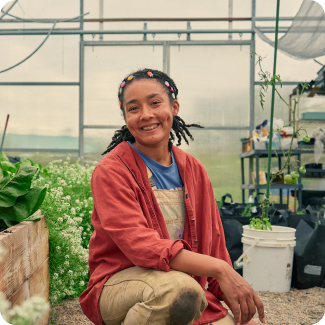 A young female farmer wearing overalls works in her greenhouse