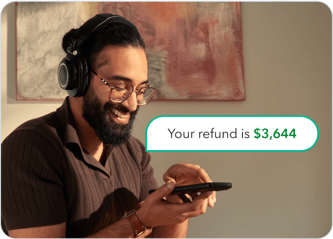 A young South Asian man in his home setting while looking at his smartphone. A text bubble next to the phone reads: “Your refund is $3,644”.