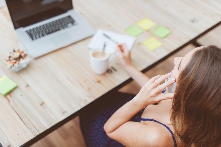 Una mujer con un teléfono en la mano, tomando un café en su escritorio.